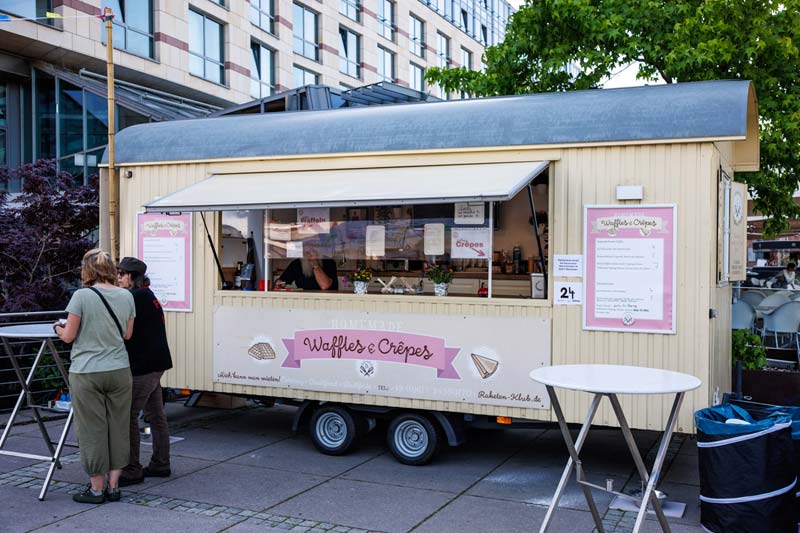 Waffel Wagen in Beige vor dem zwei Personen an einem Bistro-Tisch essen