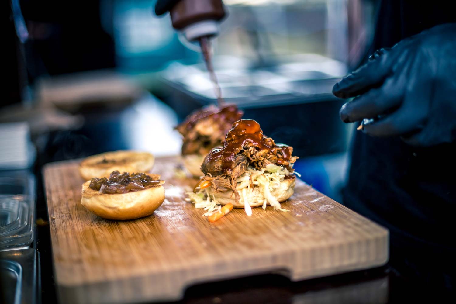 Jemand schüttet Soße auf einen Hamburger-Patty auf einem Holzbrett